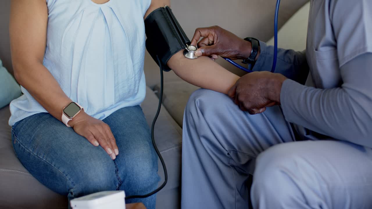 Clinico e paziente che controllano la pressione sanguigna e monitorano i parametri vitali durante una visita a domicilio, usando un bracciale e uno stetoscopio.