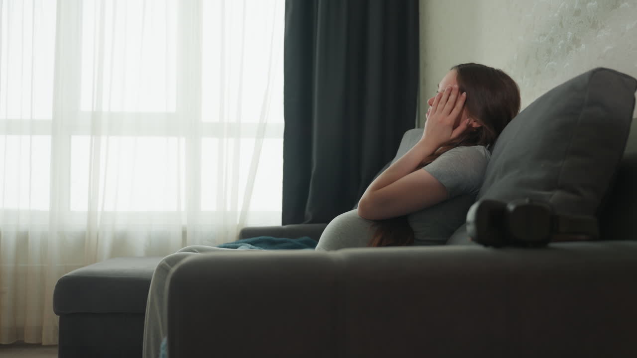 Una donna in attesa riposa serenamente in una stanza accogliente. Una donna incinta seduta dolcemente con un'illuminazione soffusa all'interno. Una donna in attesa si gode un momento tranquillo seduta comodamente nel suo soggiorno