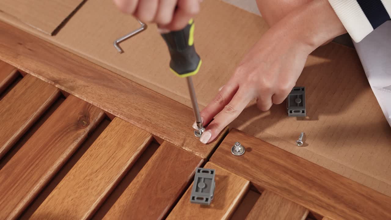 Hands assembling wooden furniture using a screwdriver and screws. Bright lighting highlights precise movements and detailed craftsmanship