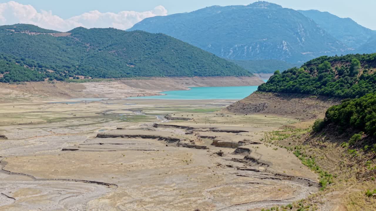 Drone passes over cracked dry lakebed surrounded by mountains in summer near Mornos, Greece