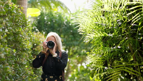 blonde photographer taking photos in tropical garden setting with dslr camera, 4k resolution, slow motion