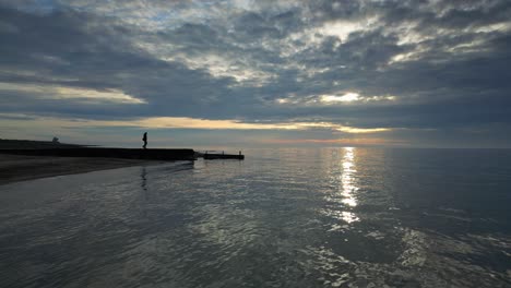 ondas suaves en cámara lenta con una silueta de hombre caminando hasta el final del muelle al atardecer en la playa de fleetwood, lancashire, reino unido