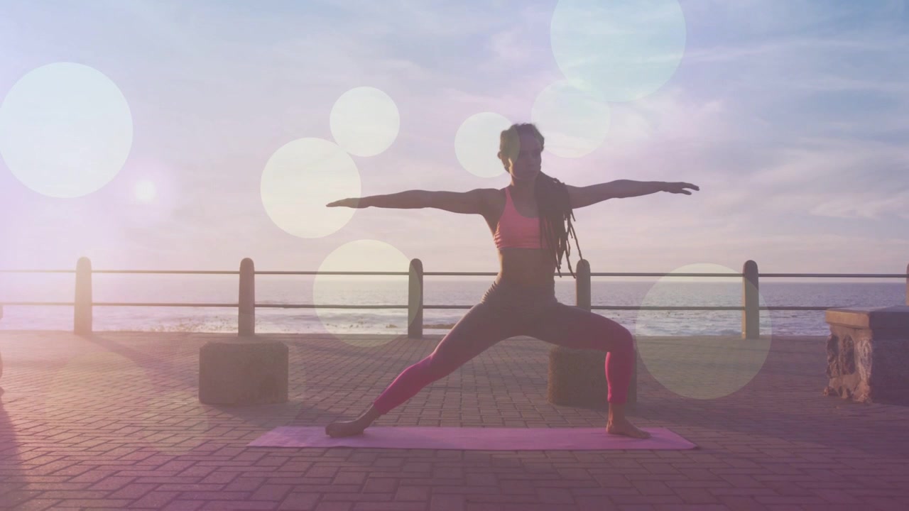 Yogini che assume una posizione su un tappetino rosa in riva all'oceano, con il sole che crea un bagliore e mette in risalto la forma fisica
