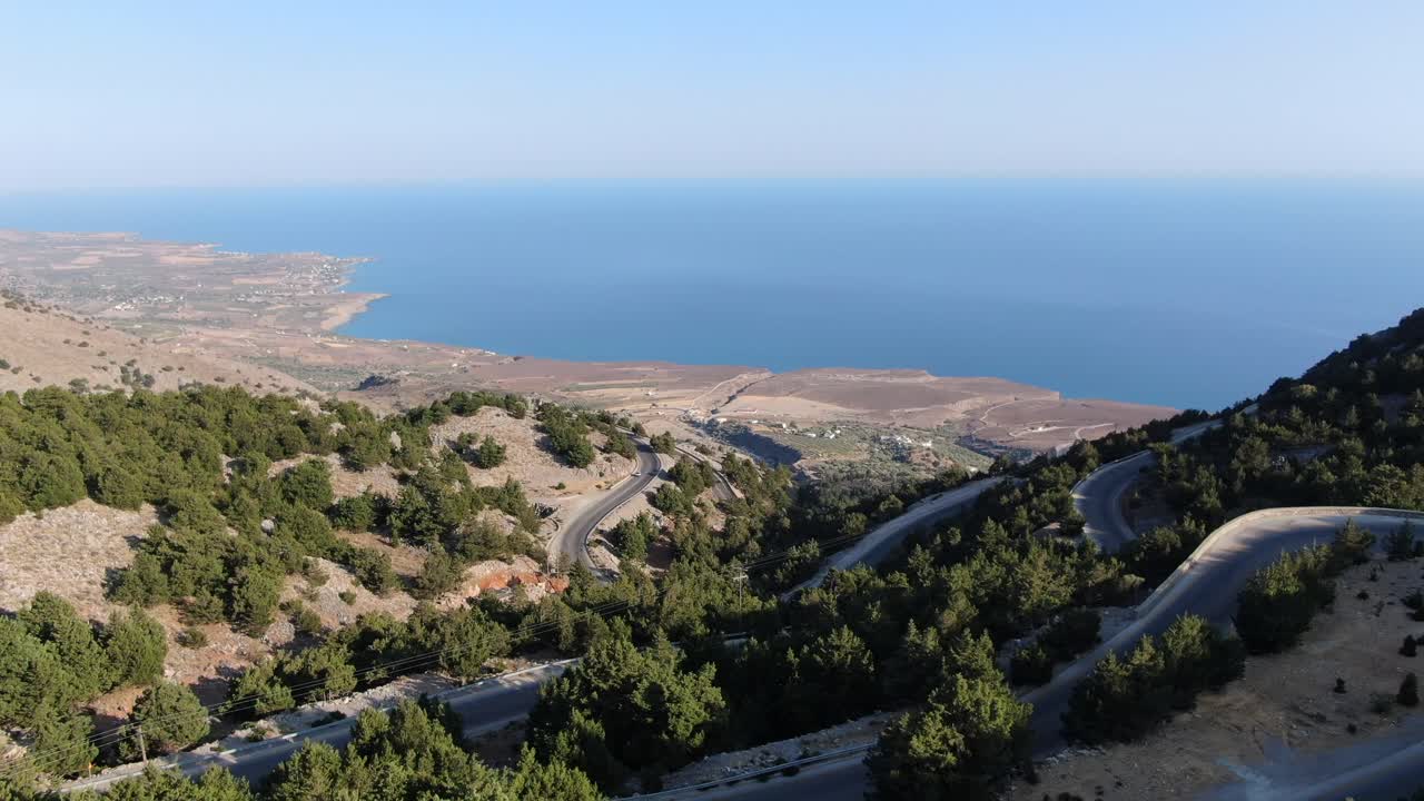 vista de avión no tripulado en grecia volando sobre una montaña marrón y verde con carretera de serpiente y mar en el horizonte en un día soleado