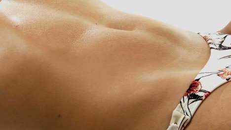 el estómago de una mujer respirando mientras usa la parte inferior de un bikini