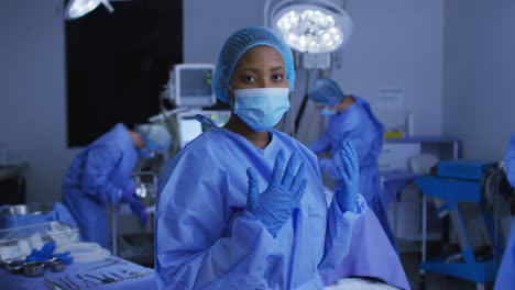 african american female surgeon wearing face mask and protective clothing in operating theatre