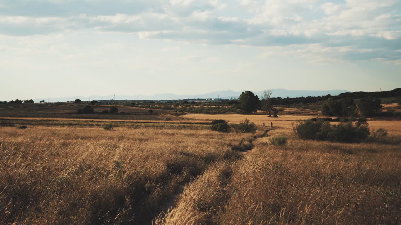 sendero vacío al atardecer con una pareja montando en bicicleta y montañas al fondo