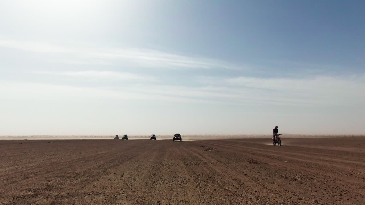 Off-road vehicles racing in the desert, kicking up dust under bright daylight