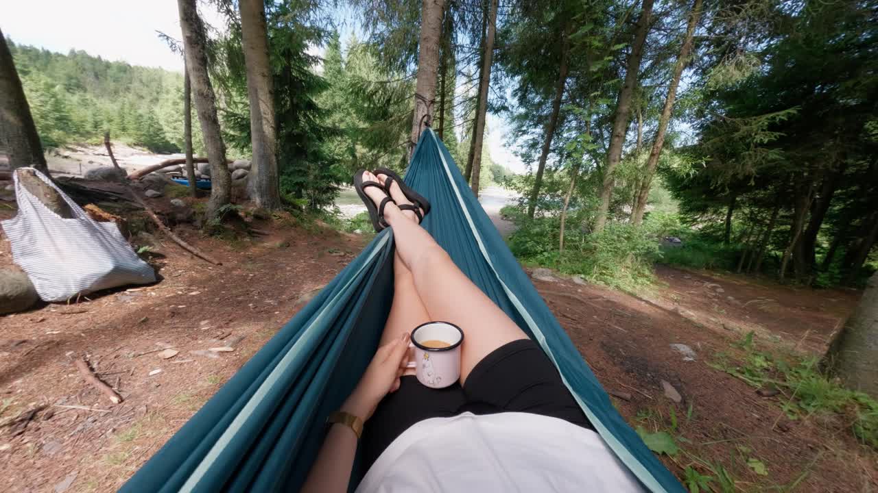 First person view of woman relaxing in hammock with coffee in forest