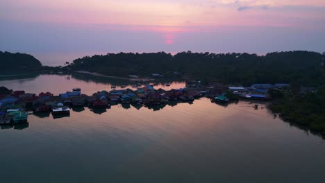 Bang Bao Pier close up, traditional fishing stilt houses reflecting on calm sea at sunset in Koh Chang, Thailand. Dramatic aerial view flight fly push forward drone