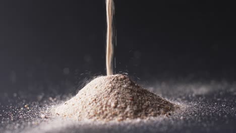 Video-of-close-up-of-sand-grains-pouring-into-heap-and-copy-space-on-black-background