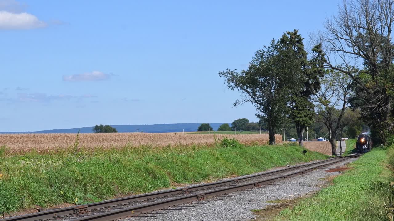vista de un tren de pasajeros a vapor que se acerca lentamente a lo largo de una sola vía en la américa rural en un día de otoño