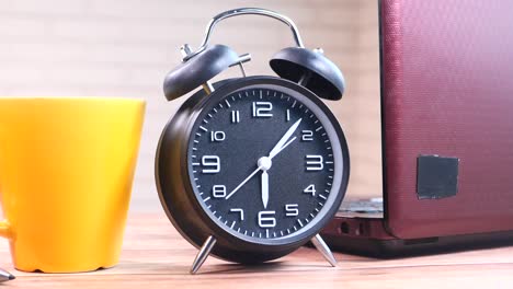 alarm clock, laptop, and coffee cup on a desk