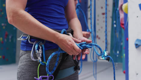 midsection of caucasian woman knotting rope in a harness belt at indoor climbing wall