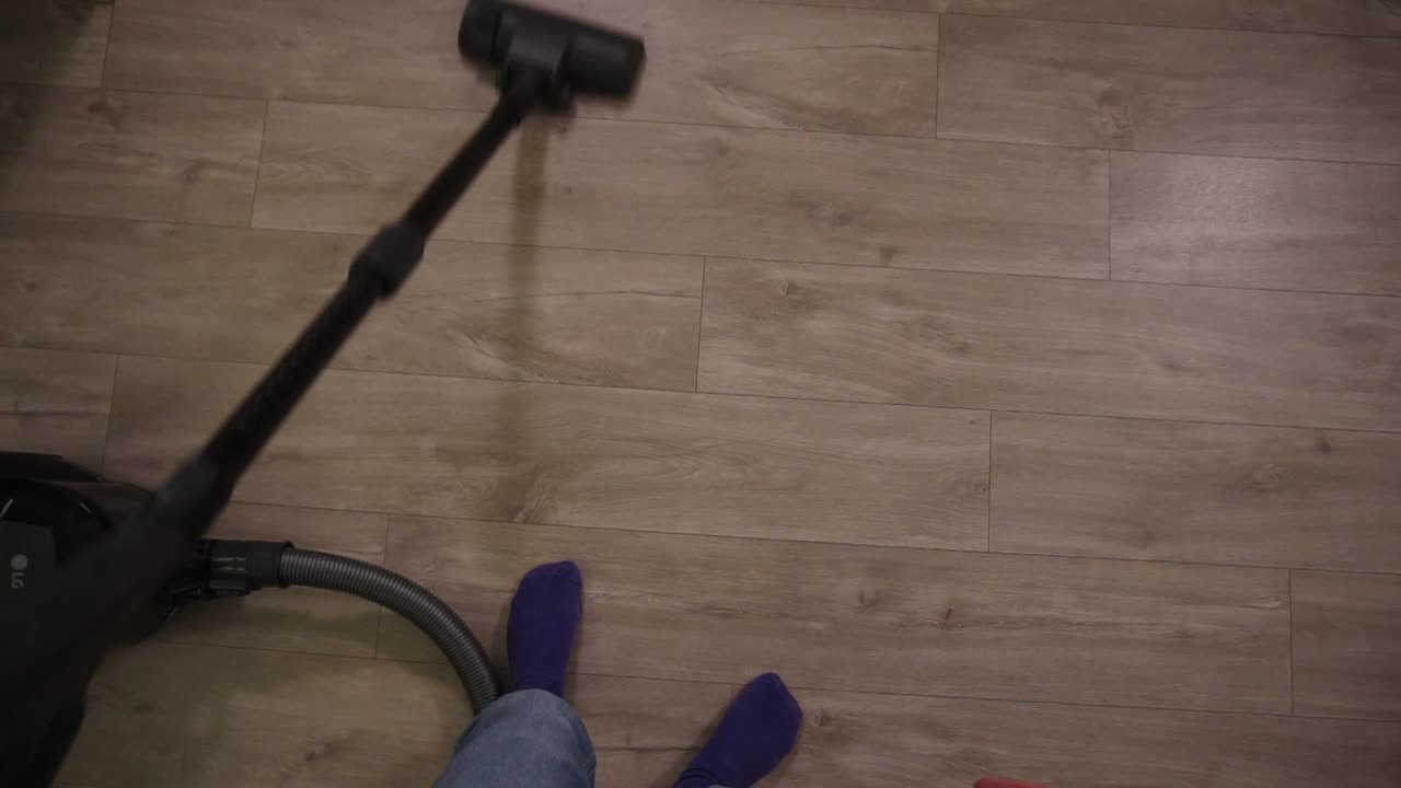 Cropped footage of a woman's legs vacuuming floor in kitchen, focused on cleaning in apartment, holding pipe. Housekeeping, lifestyle and creative people concept. Slow motion. Top view