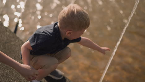 Boy-touches-fountain-spray-holding-mother-hand-in-city