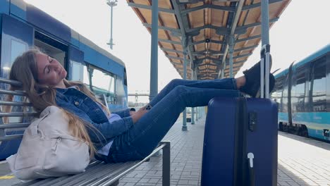 a woman sleeps on the platform of the railway station with luggage, she is waiting for her train. tired female tourist