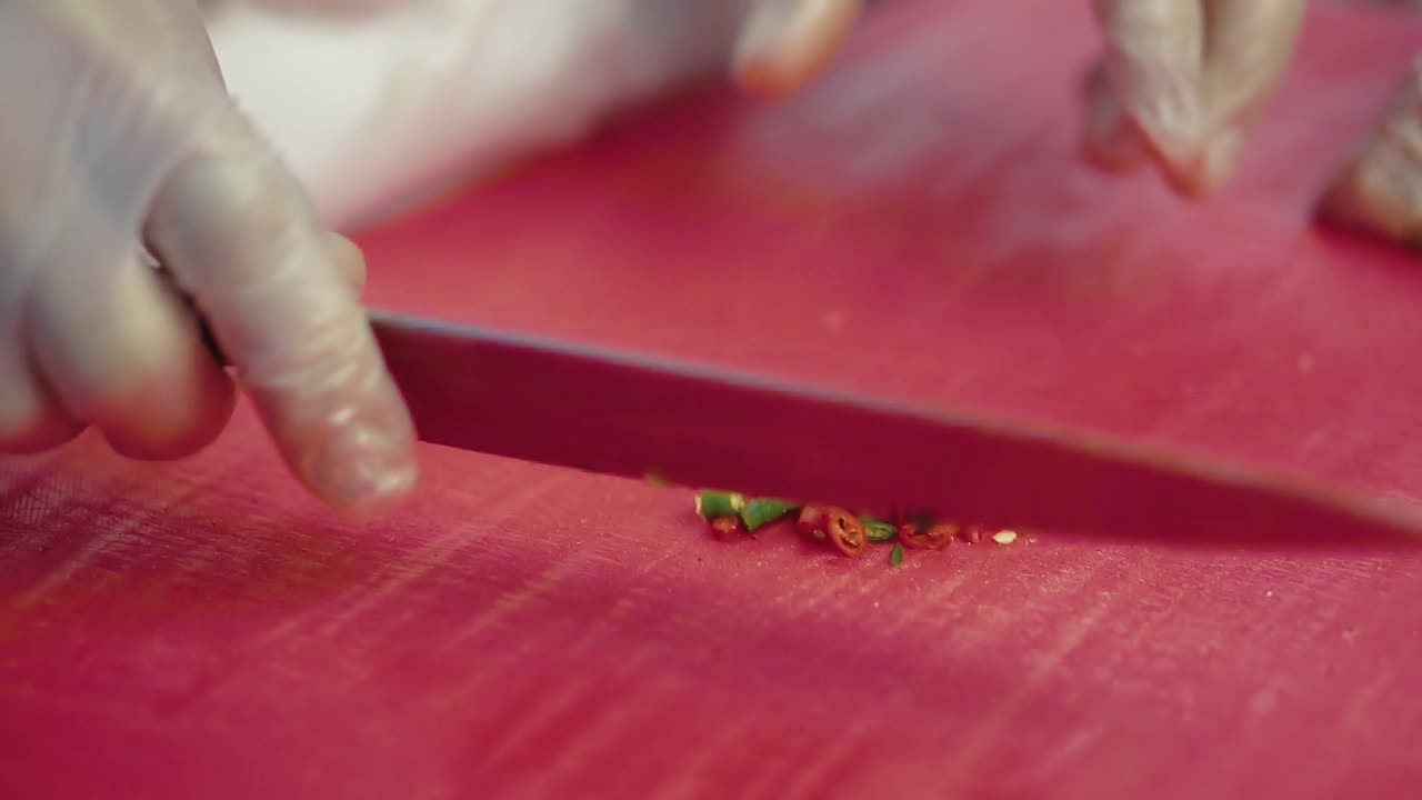 повар нарезает перец чили для салата