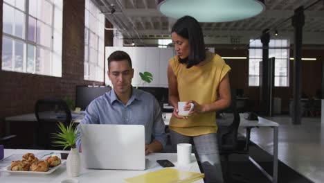 diversos colegas de negocios masculinos y femeninos en una discusión usando una computadora portátil sosteniendo una taza de café