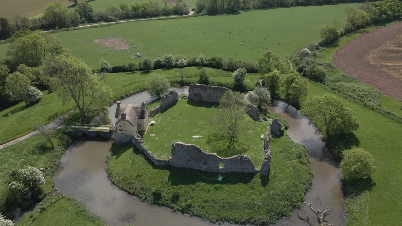 Aerial view of Stogursey Castle, a medieval castle in Somerset, England. Most of the site is in ruins, with a thatched gatehouse used for holiday's. Drone rotating to the right over the ruins and moat