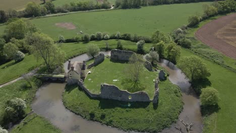 aerial view of stogursey castle, a medieval castle in somerset, england. most of the site is in ruins, with a thatched gatehouse used for holiday's. drone rotating to the right over the ruins and moat