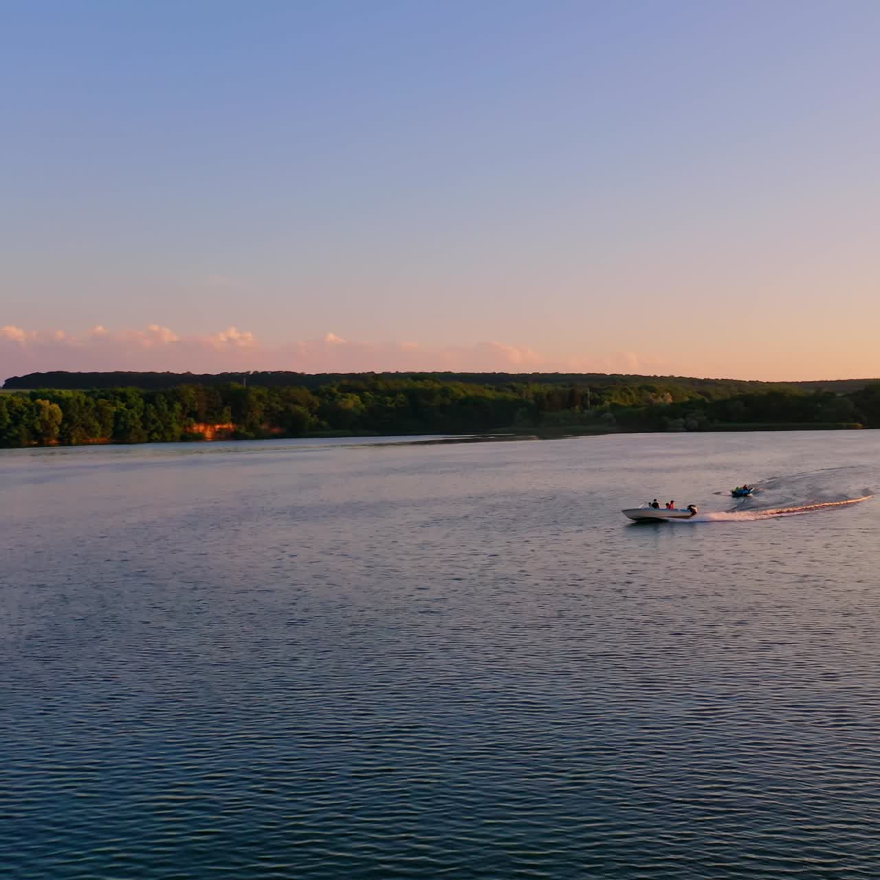 Beautiful evening landscape over the water. Motor boat floating at orange sunset. People travelling in high-speed boat under clear sky.