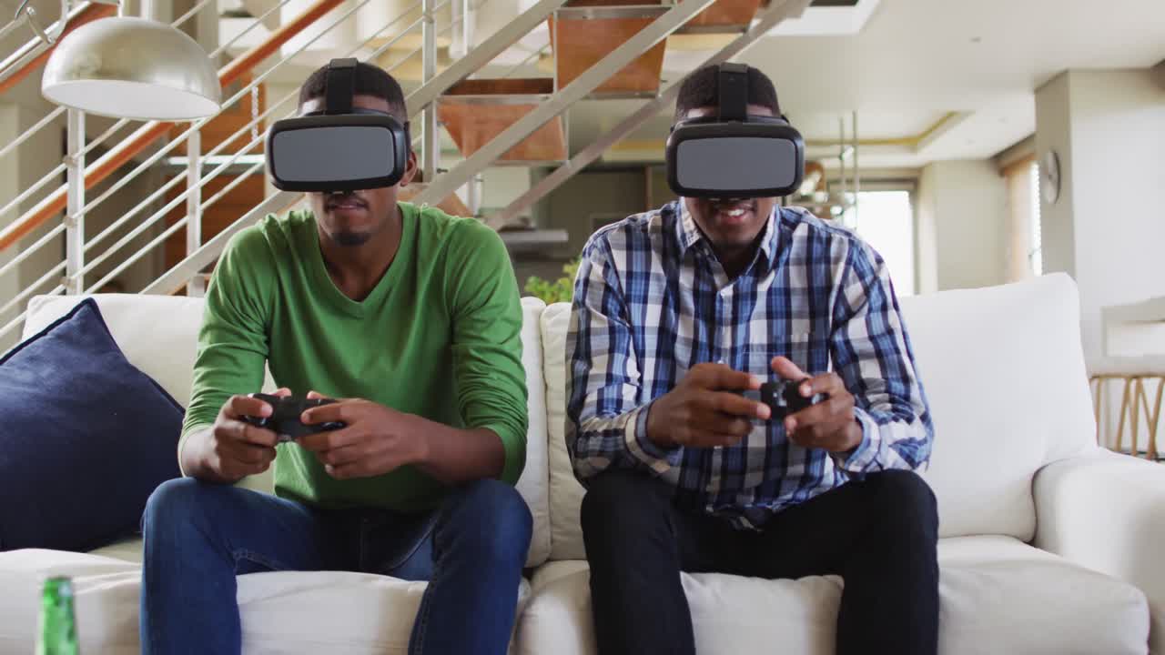 Fratelli gemelli adolescenti afroamericani sul divano che usano visori VR e giocano a un videogioco sorridendo