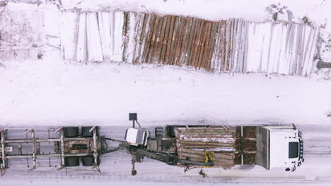 truck mounted log loader places pile of logs onto truck in snow