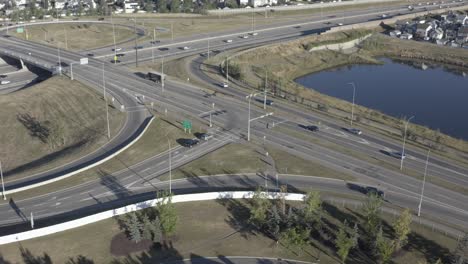 Antenne-Am-Frühen-Morgen-über-Sonniger-Sommerautobahn-Autobahnausfahrt-Eingang-Zum-Anschluss-Des-Wichtigsten-Stadtknotenpunkts-Von-Wohnhäusern-Zu-Geschäftsstraßen-Rund-Um-Plätzchen-Geschnittene-Häuser-Künstlicher-Künstlicher-Teich-2-3