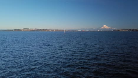 A-lone-sail-boat-in-Commencement-Bay-of-the-shore-of-Tacoma-Washington,-Mount-Rainier-and-the-tide-flats-in-the-background