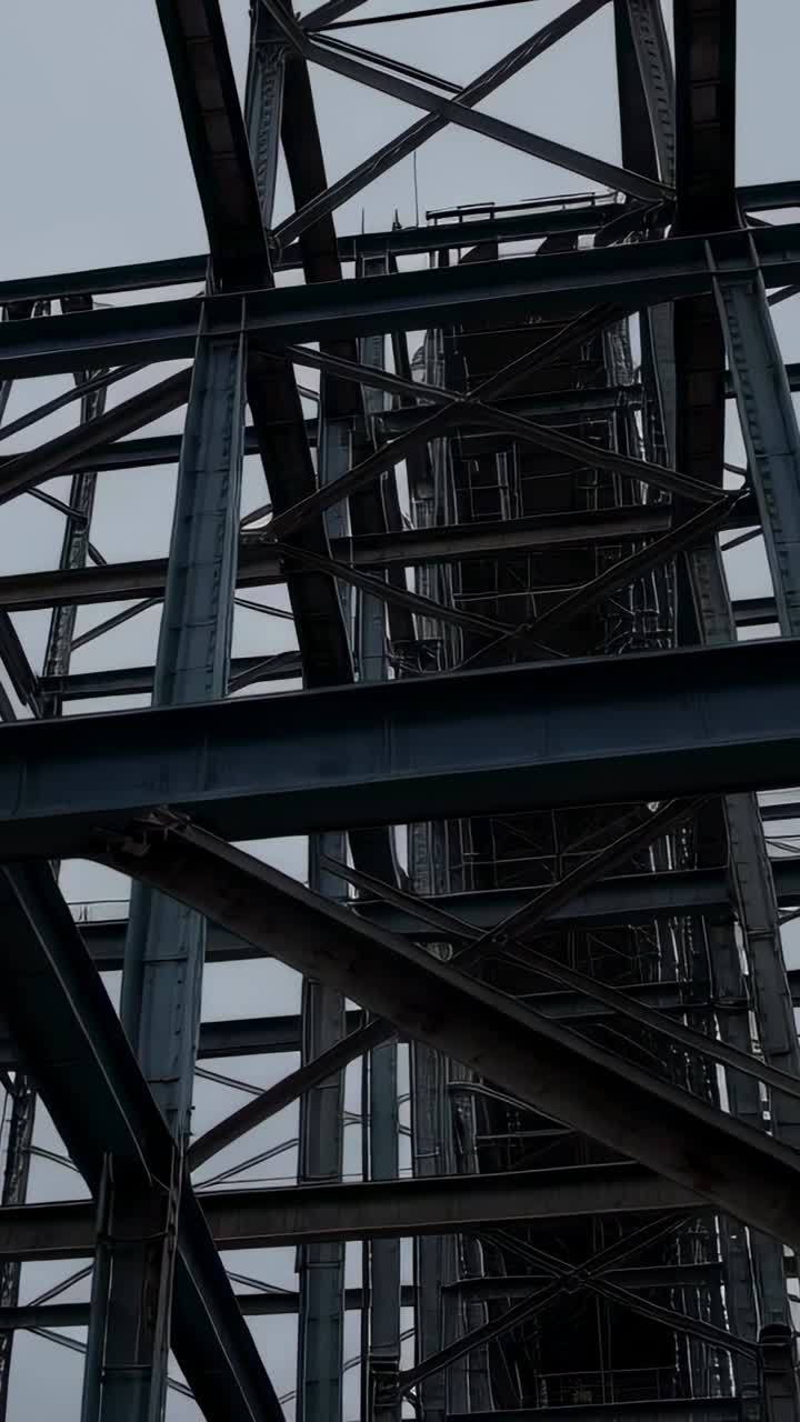 Vertical video: Tilting camera revealing steel truss beneath bridge to show central access shaft