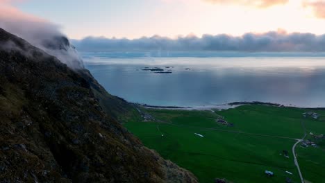aerial near mannen wall reveals utakleiv and mountain top wrapped in ocean fog at midnight sun