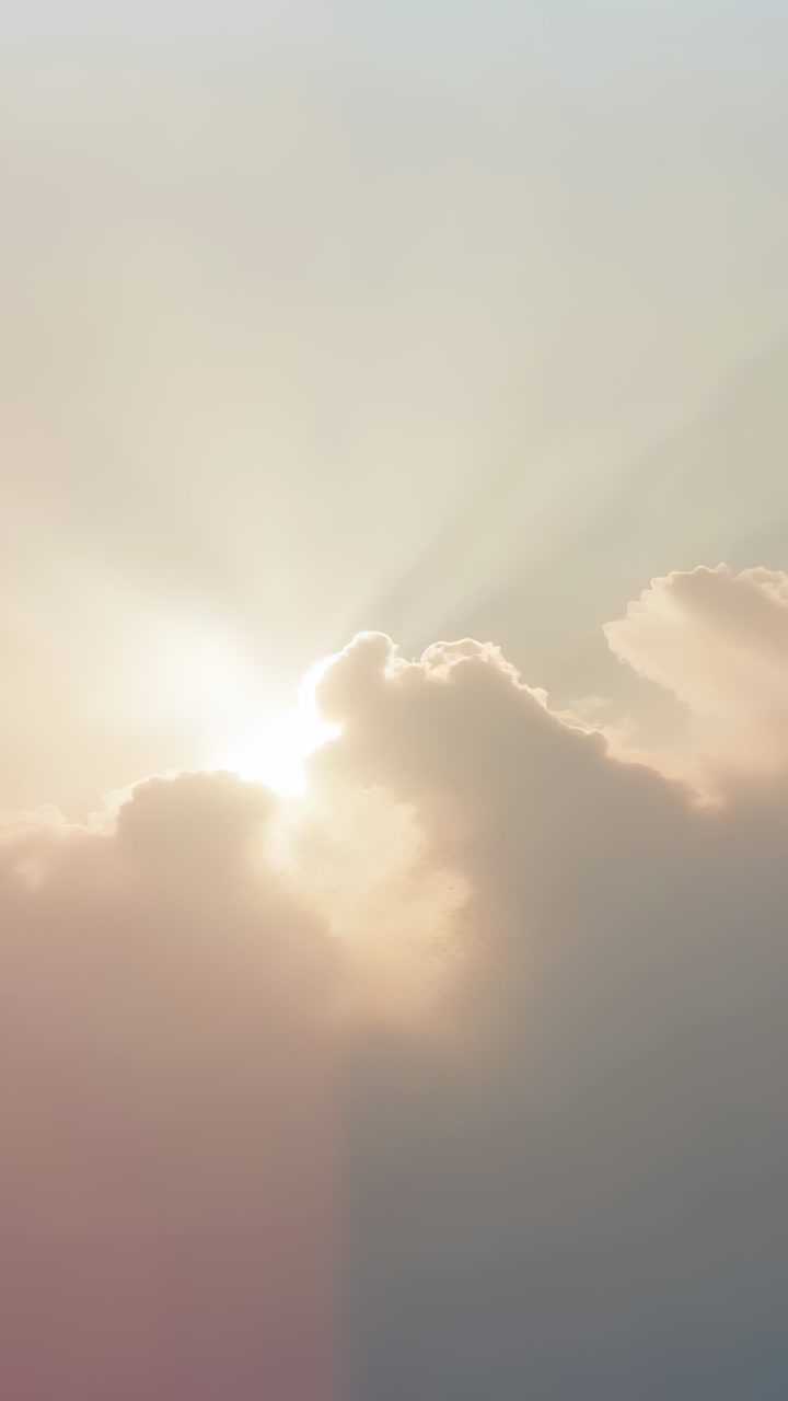 Vertical video: Peeking sun sliding past scalloped cloud edge in sky as clouds shift, forming beams