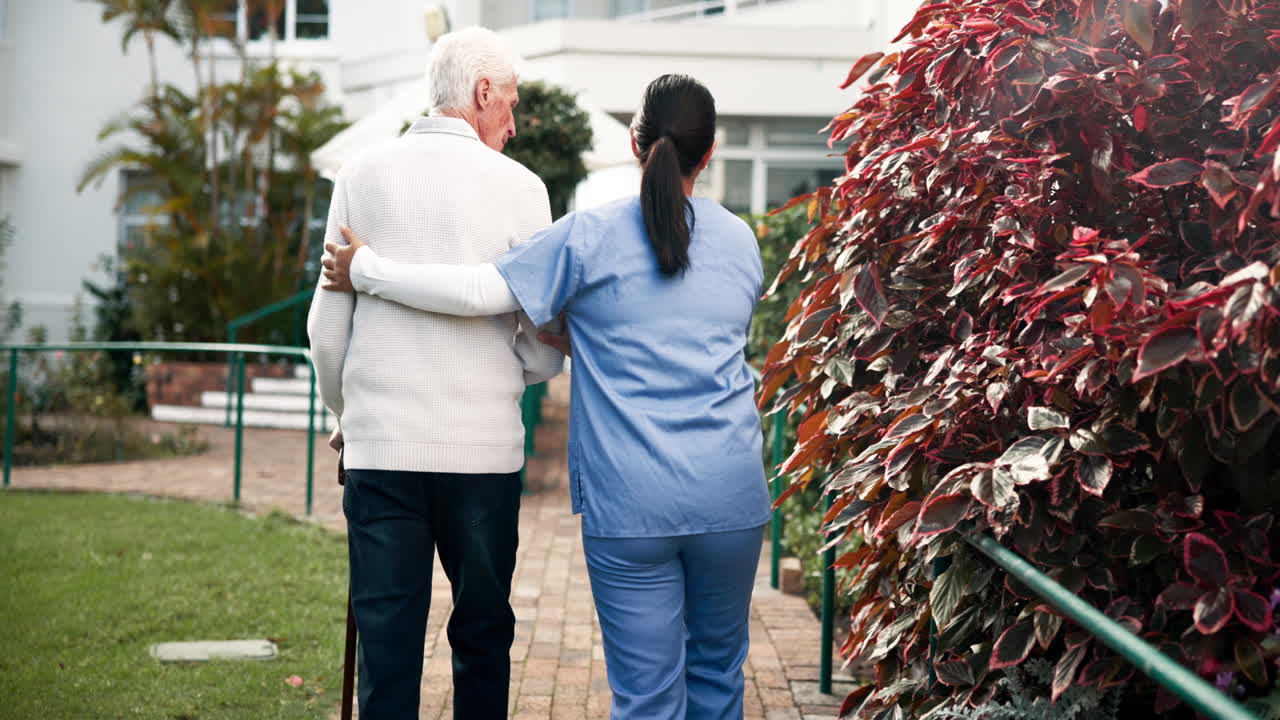 Nurse assisting senior man walking in garden