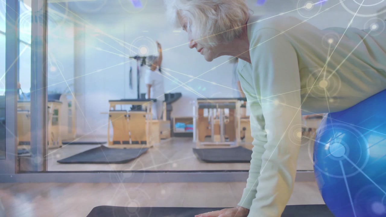 Senior woman leaning on blue stability ball in Pilates studio, showing animated workout stats