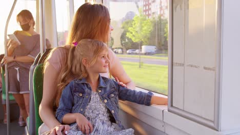 Family-rides-in-public-transport,-woman-with-little-child-girl-sit-together-and-look-out-window-tram