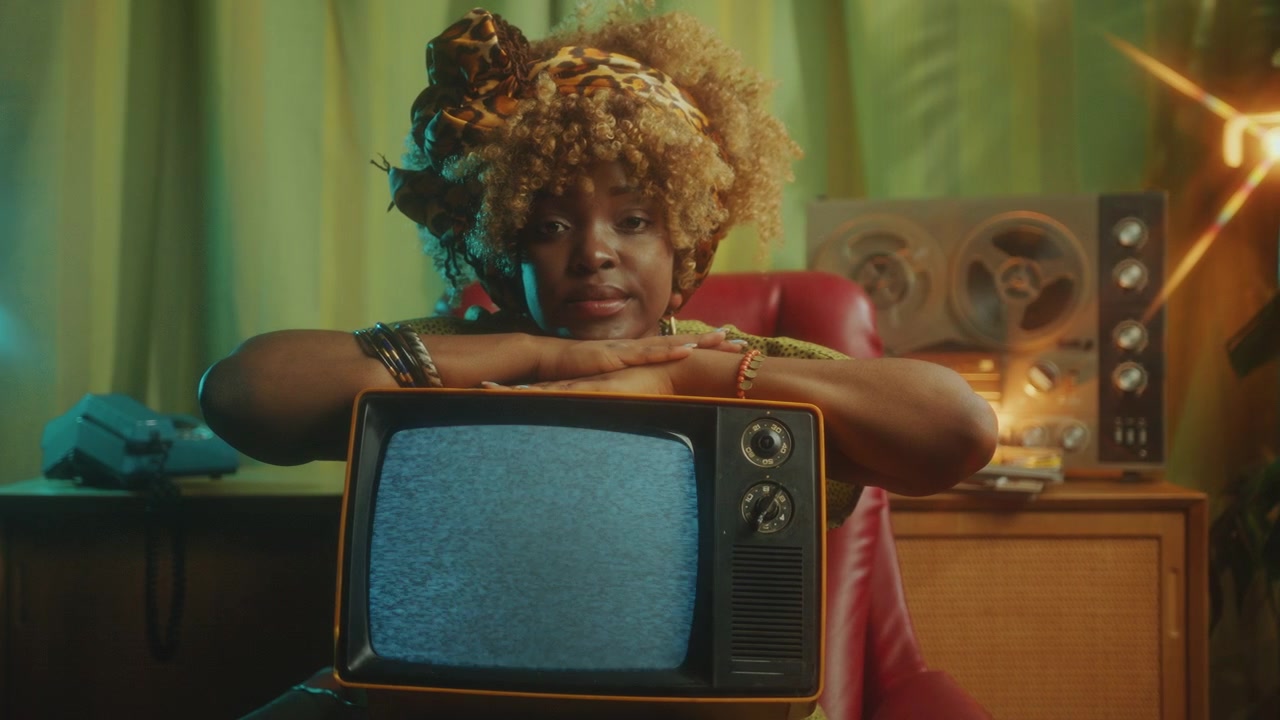 Ritratto di una bella donna afroamericana con una TV retrò in uno studio vintage