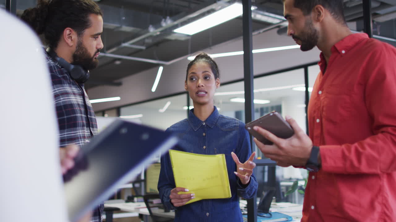 grupo diverso de colegas de trabajo de pie sosteniendo documentos y hablando en tableta