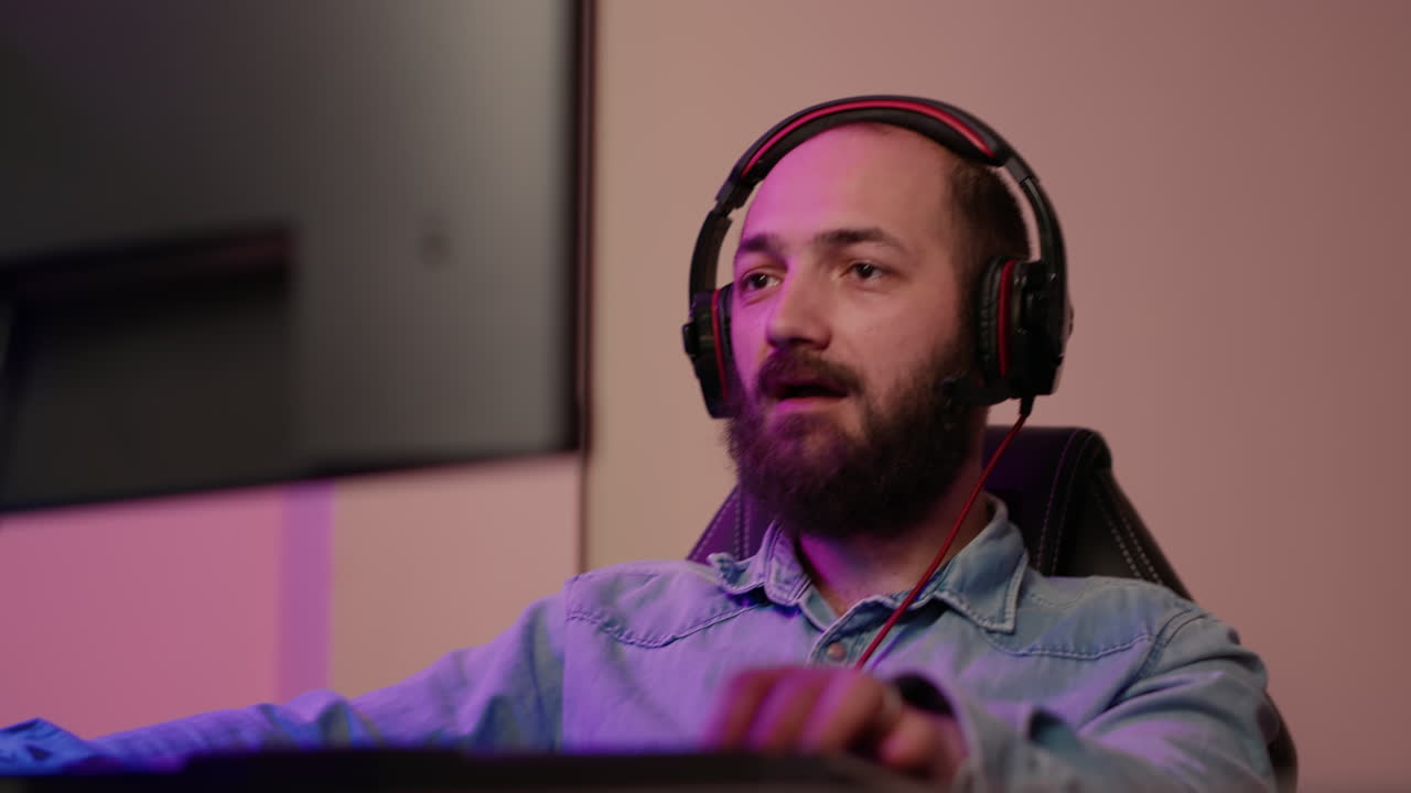 Handheld shot of man with gaming headset looking at computer screen and talking to team members