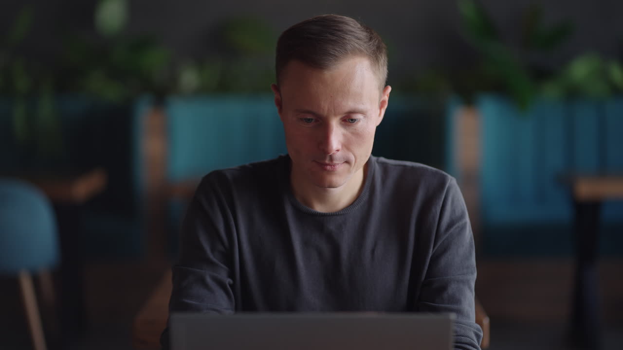 Handsome freelancer businessman in glasses diligently working on laptop in cafe. Man typing on keyboard and searches new job on internet at coffee shop. Business concept