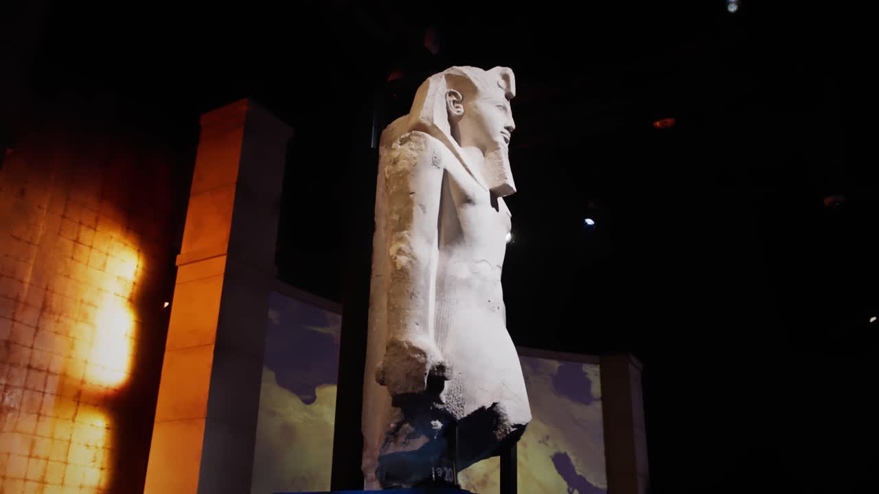 Sideprofil av en monumental statue av Ramses II utstilt i et mørkt museum, dramatisk belyst med linseglimt og en oppslukende historisk bakgrunn.