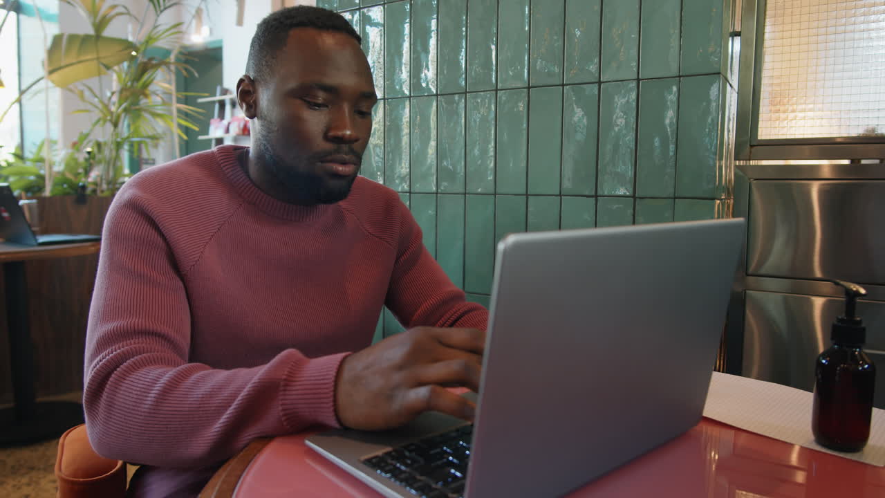 African American Man Typing on Laptop at Cafe Table