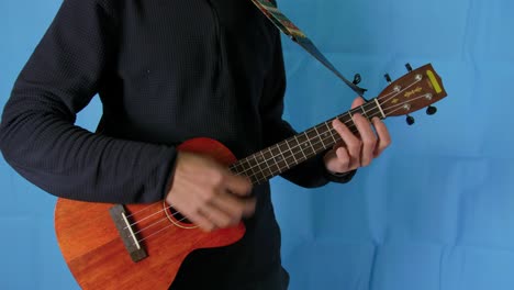 static close up of a musician man playing ukelele with blue studio background