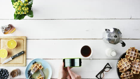 Top-view-man-looking-at-big-data-graphs-using-smartphone-at-breakfast-Belgian-waffles-and-coffee-hands-from-above---Red-Epic-Dragon