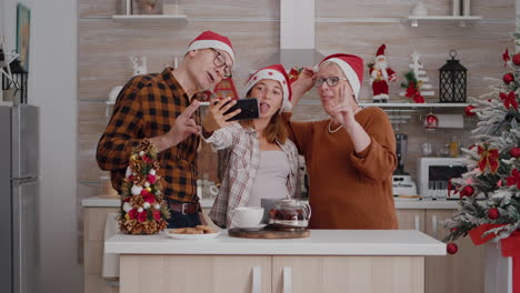 familia tomando selfies usando el teléfono inteligente disfrutando de las vacaciones de invierno en la cocina decorada con navidad