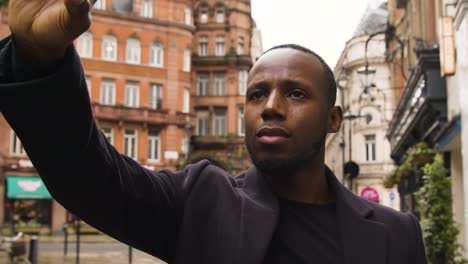 male lifting his smart phone up to take a photo on a street in london city