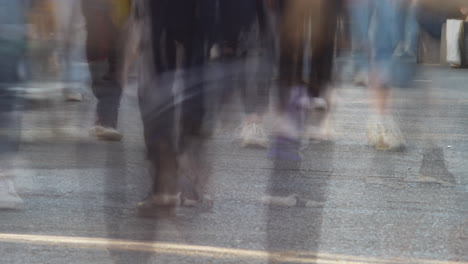 a dynamic timelapse shot captures the blurred motion of unrecognizable people walking and cycling on an urban street, from a low perspective focused on feet and pavement