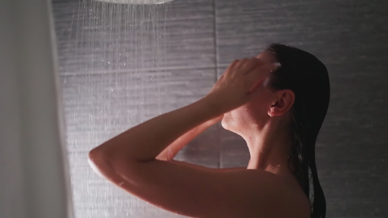 샤워 객실에서 은 머리카락을 만지는 여성: 사려 깊은 여자가 집 화장실에서 따뜻한 물로 머리카락과 몸을 습니다.