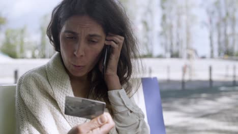 mujer madura enfocada con tarjeta de crédito y hablando por teléfono.