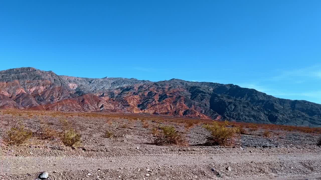 Formazioni rocciose minerali multicolori in una catena montuosa desertica. Paesaggio desertico con montagne che presentano distinti depositi minerali rossi, verdi e grigi sotto un cielo azzurro e limpido.